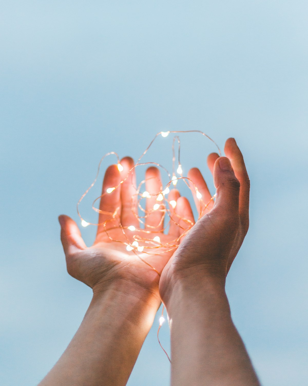 Hands gently holding glowing string lights, evoking warmth and a sense of quiet hope