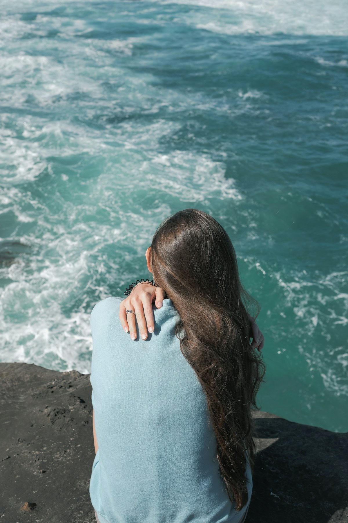 Woman sitting on a rock by the ocean in soft natural light, looking peaceful and contemplative